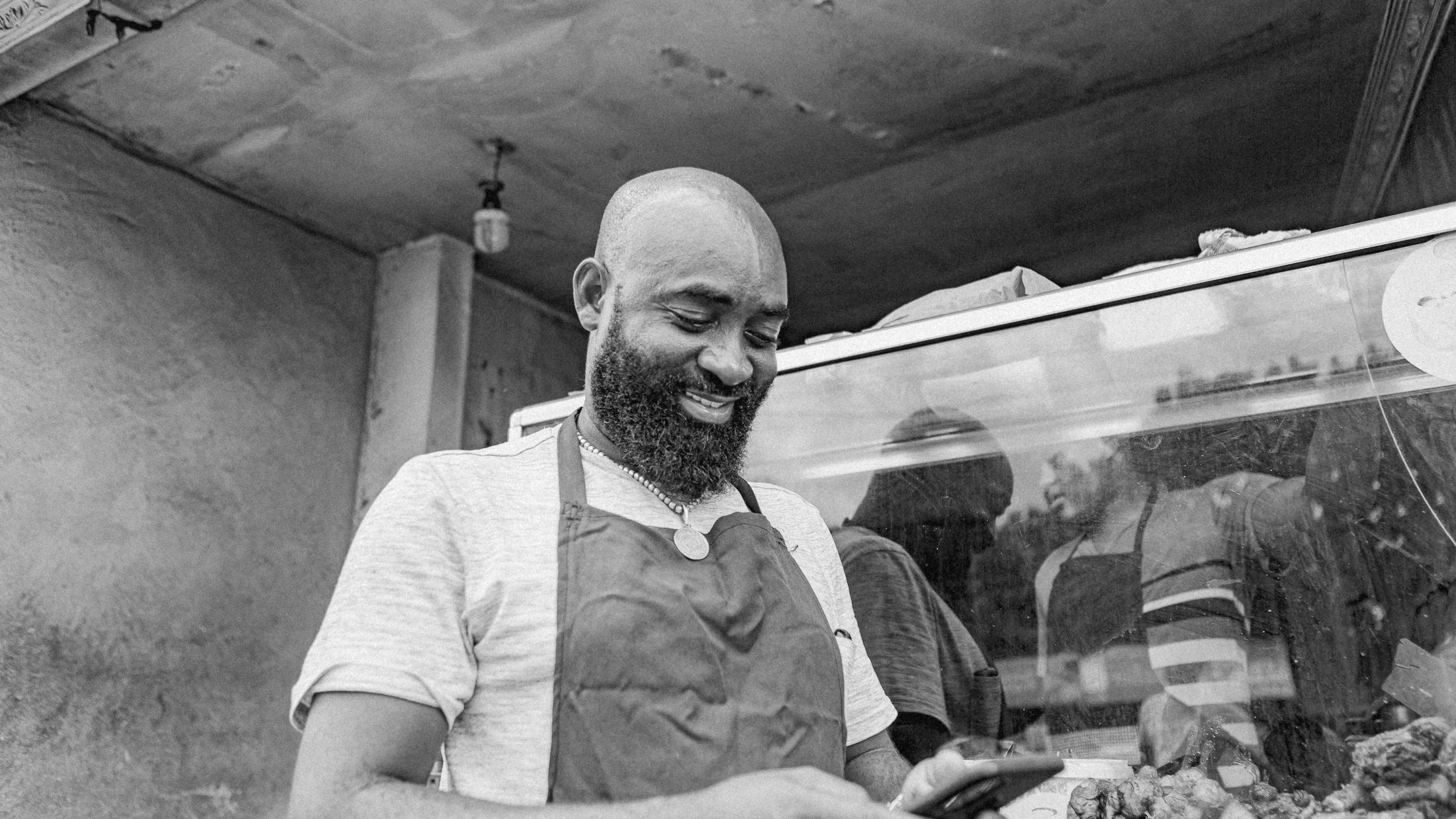 A food shop owner in an apron, smiling at his phone